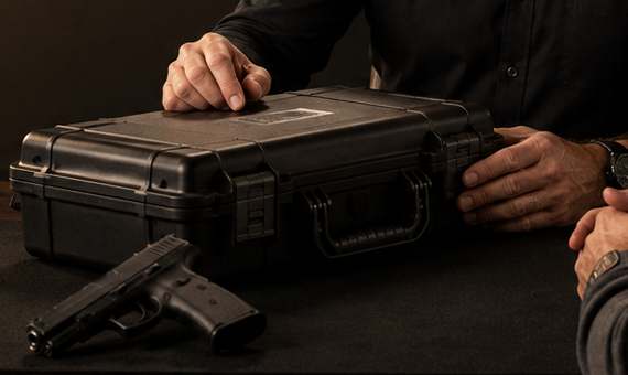 Two people passing a closed firearm hard case across a consultation table.
